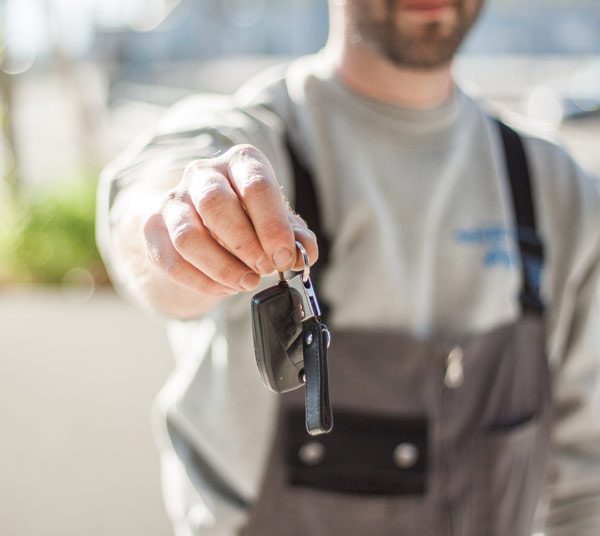 out-of-focus mechanic wearing grey overalls handing car key chain with fob