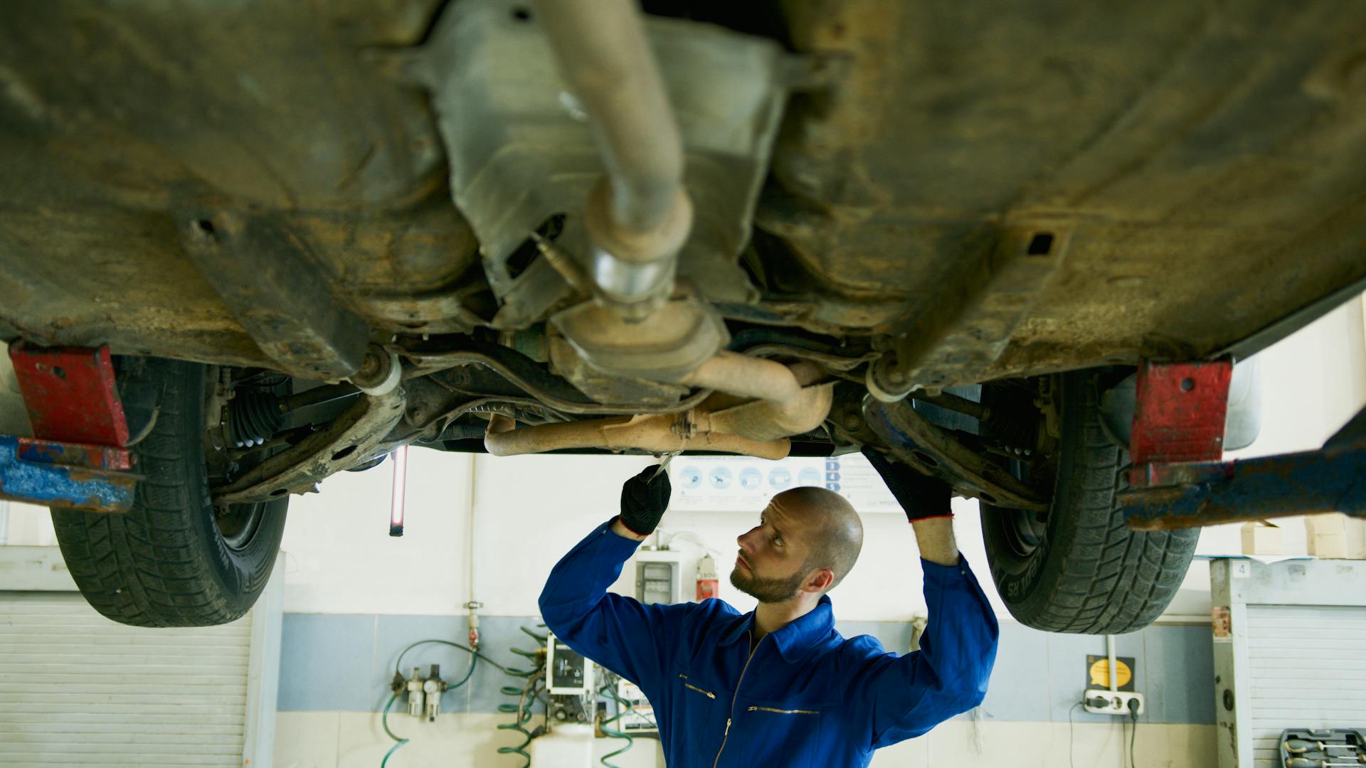 Man working underneath a car at a transmission shop performing transmission repair and inspection work.